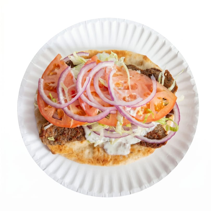 Overhead view of a gyro on pita bread with meat, tomatoes, red onions, lettuce, and white sauce.